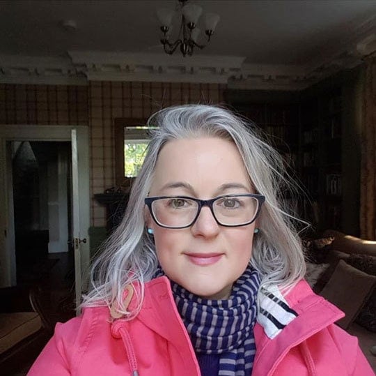 image of pretty woman pink jacket gray hair glasses