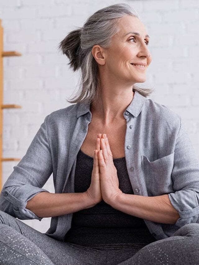 image of mature woman with gray hair in a yoga pose in a white room