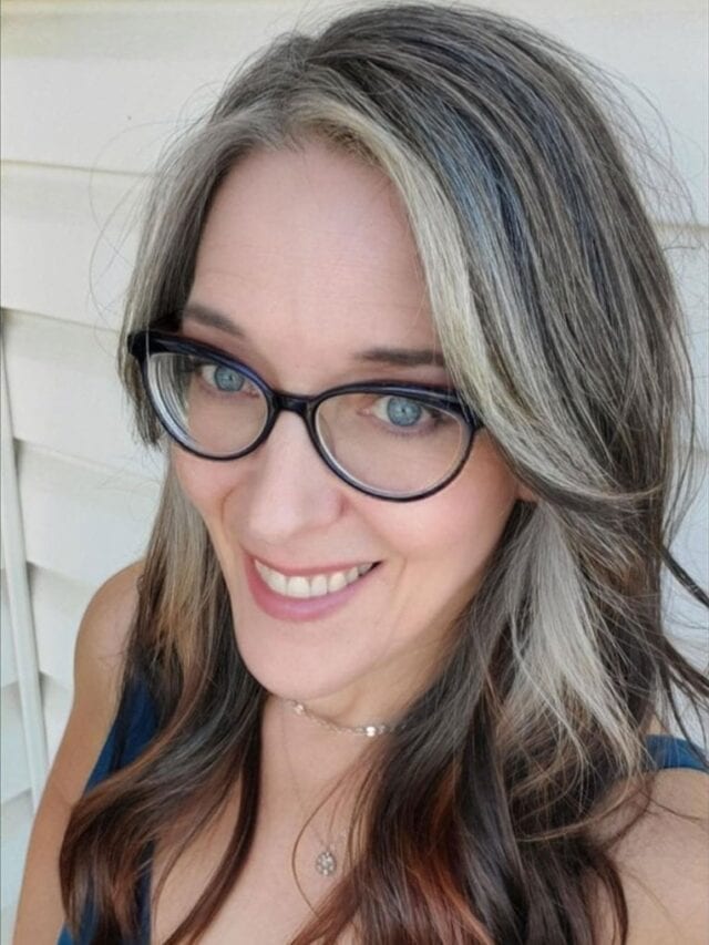 woman with black glasses and long gray hair with dark ends and dark tank top