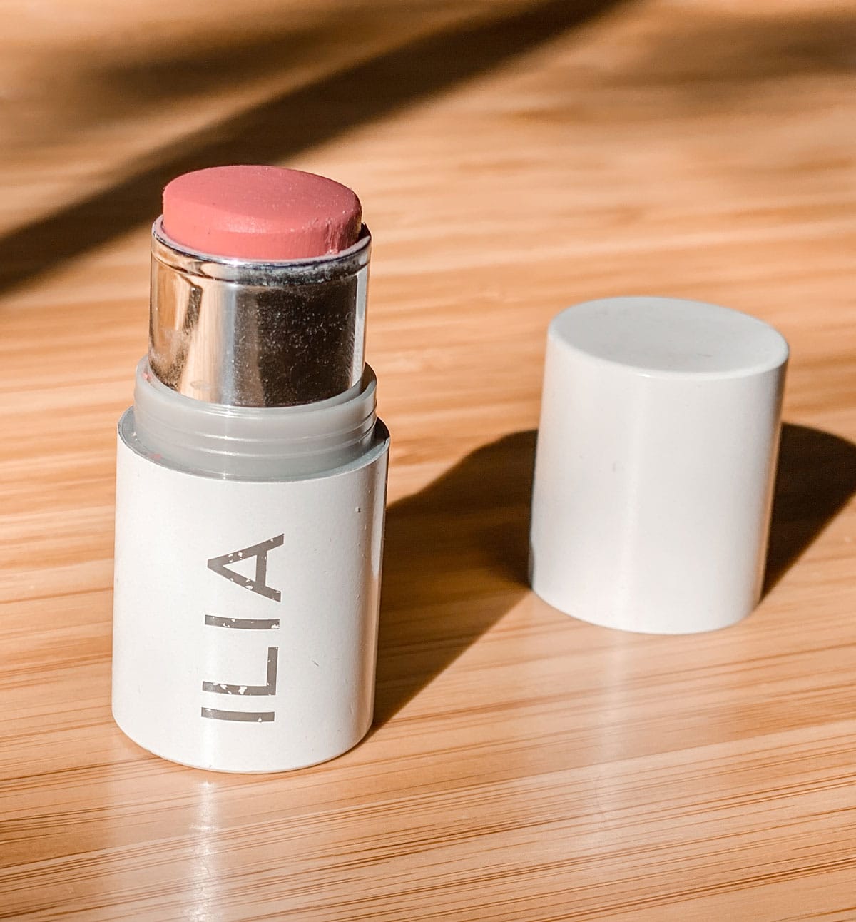 Ilia multi-stick blush open (with lid standing next to it) on a wooden table