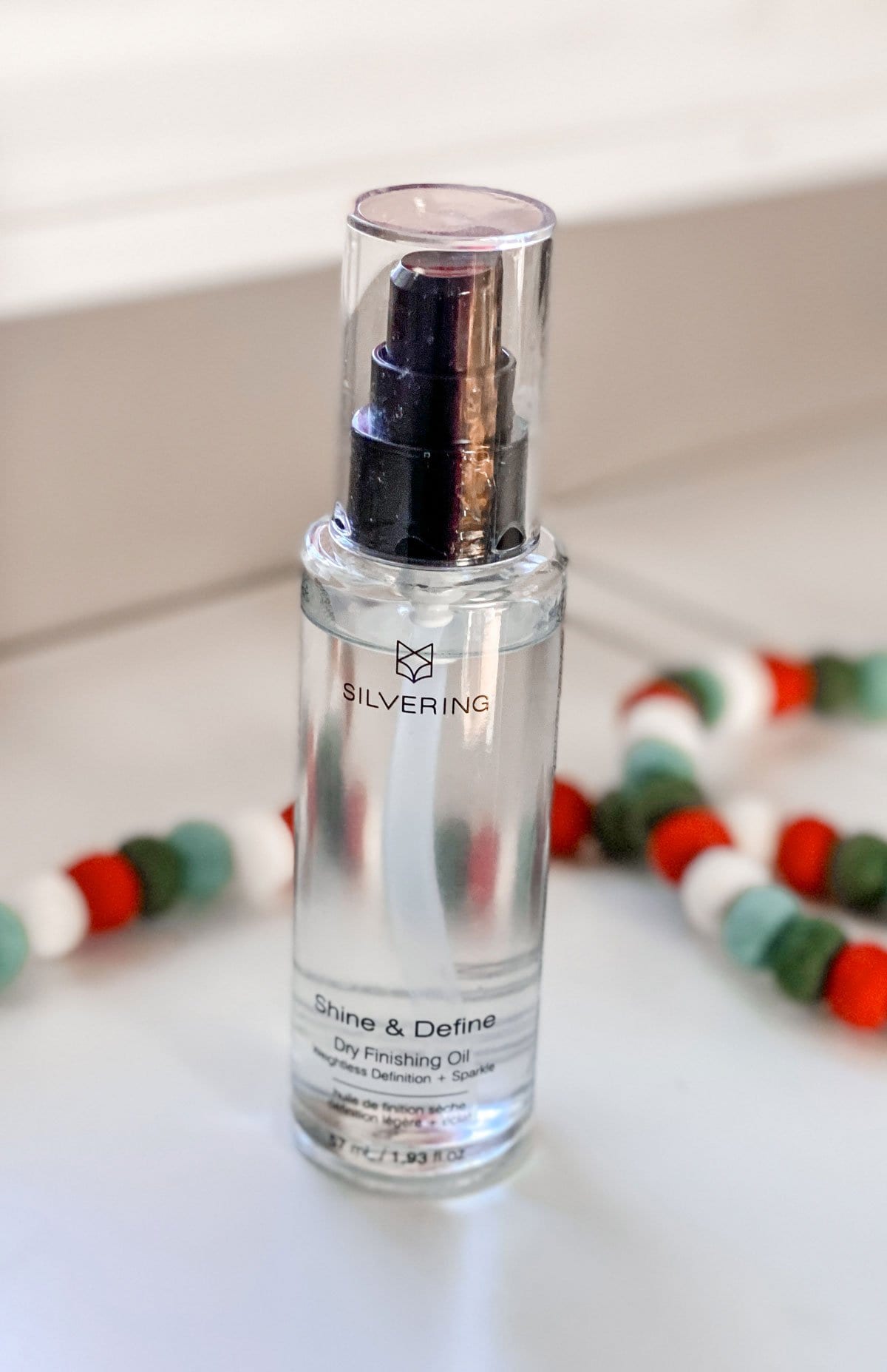 Silvering Shine and Define Dry Finishing OIl on a white shelf next to a Christmas garland