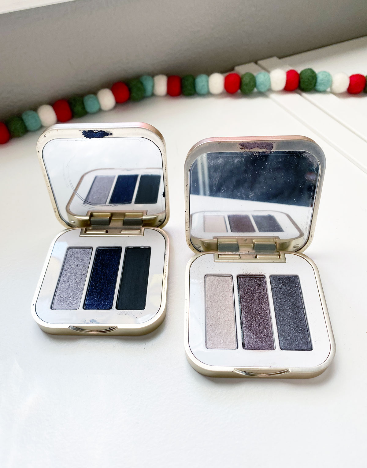 2 eyeshadow palettes on a white counter near a christmas garland