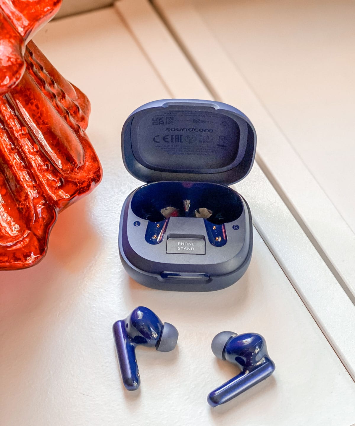 image of blue soundcore earbuds on a white surgace, next to their blue case. 