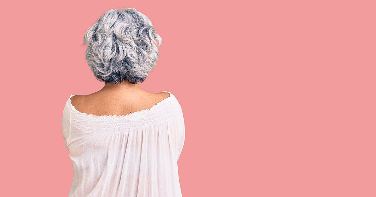 woman in white shirt with bobbed curly gray hair against pink background
