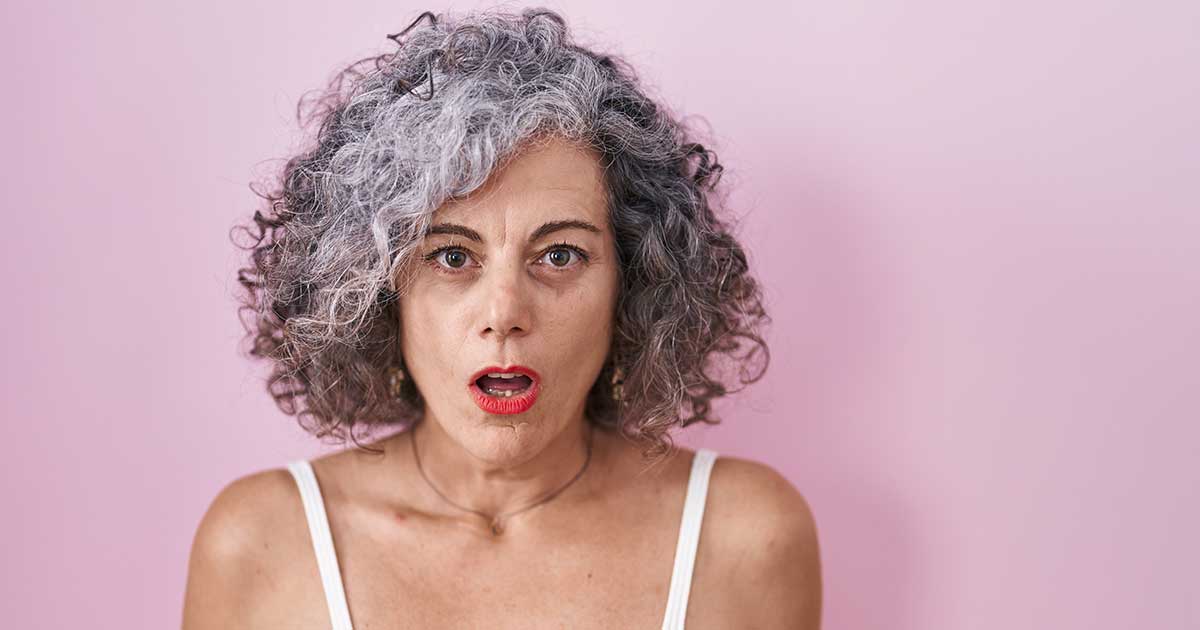 shocked woman with curly gray hair against a pink background
