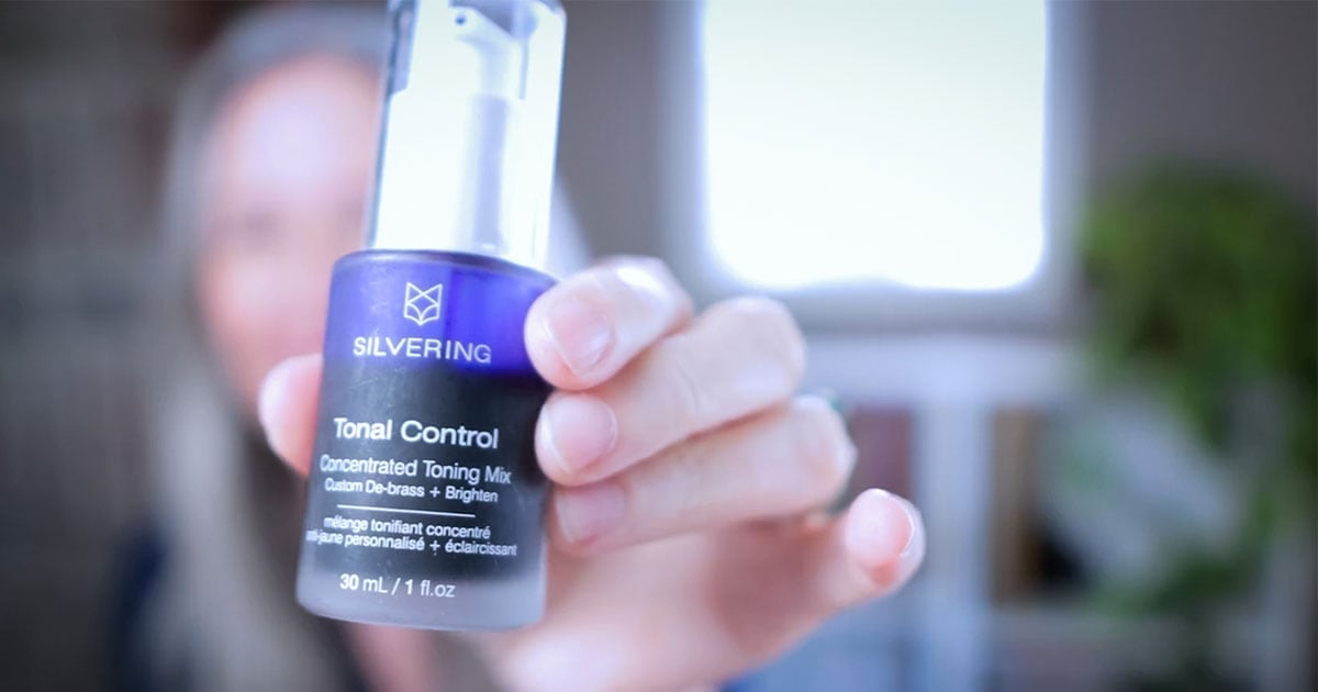 image of Katie (blurred in backgrounding) holding up a bottle of Silvering Tonal Control