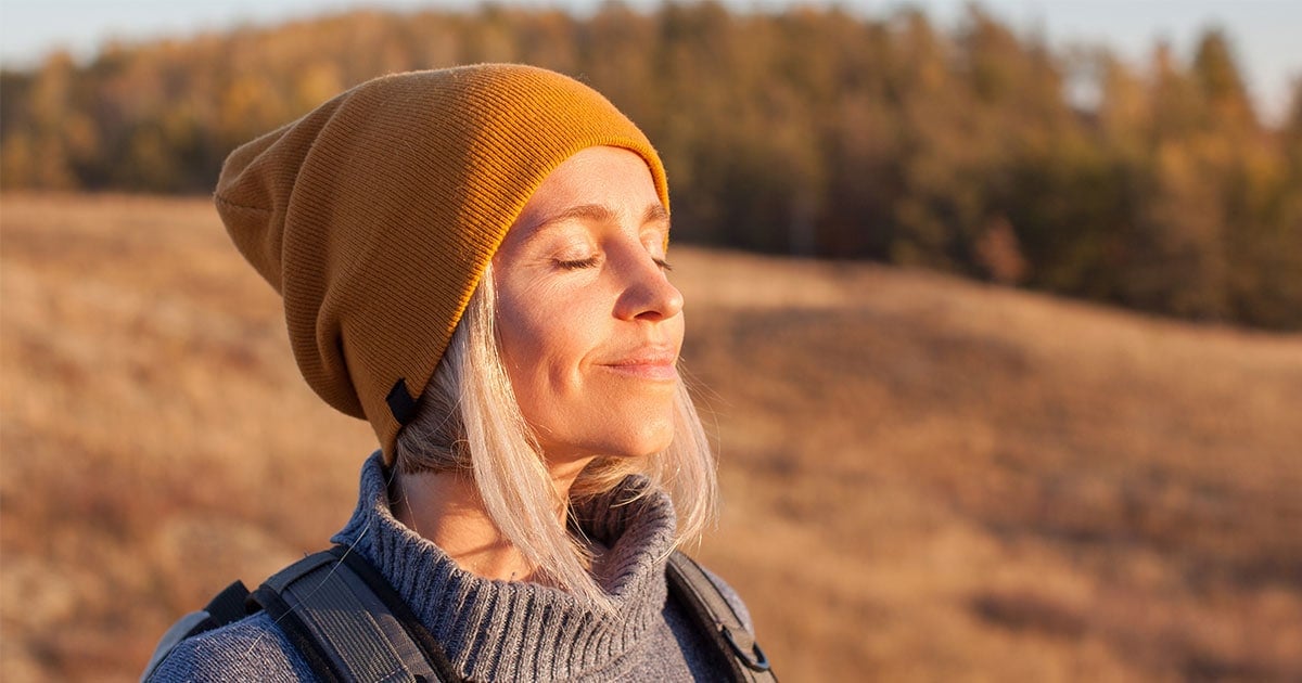 image of woman on a hike, eyes closed, face bathed in sunlight - peaceful
