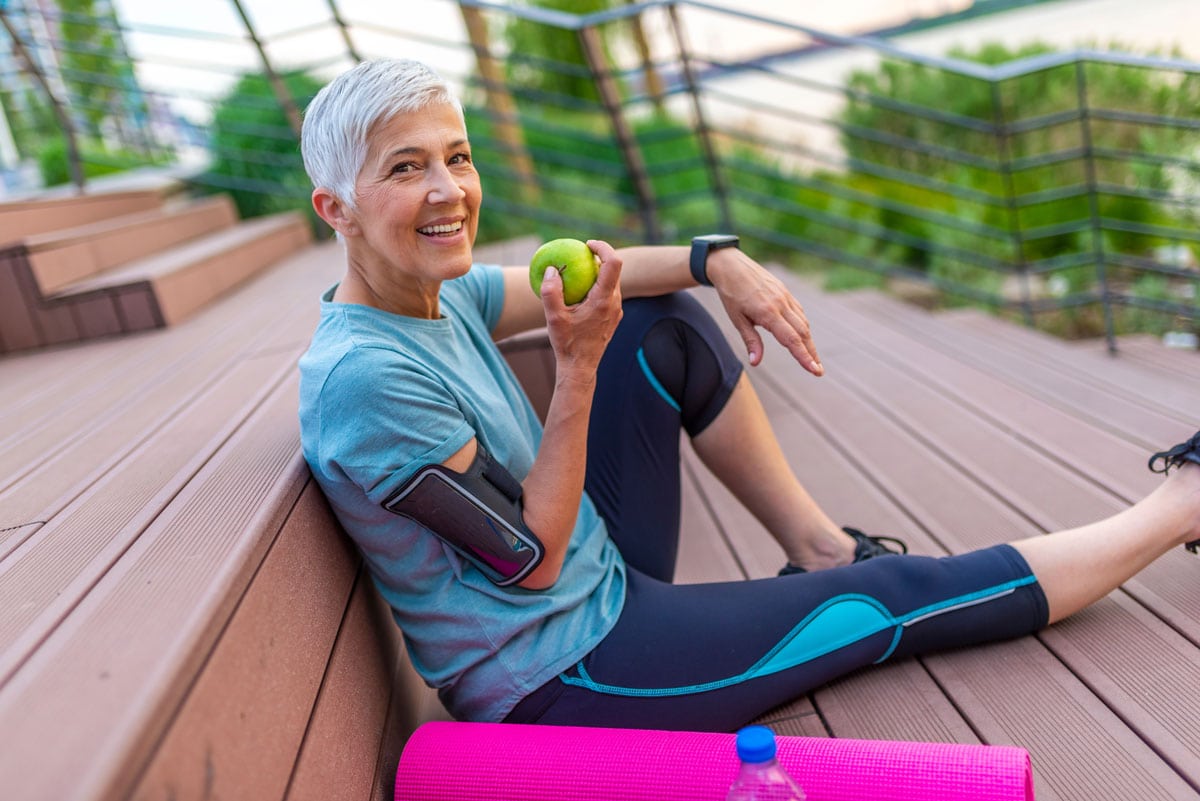 image of gray hair woman eating apple while taking a break from exercising