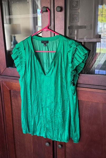 image of a green silk blouse hanging on a hanger